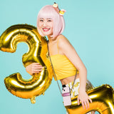 Smiling woman in yellow crop top wearing Petra store crossbody chain for smartphones with pink phone case and gold balloons