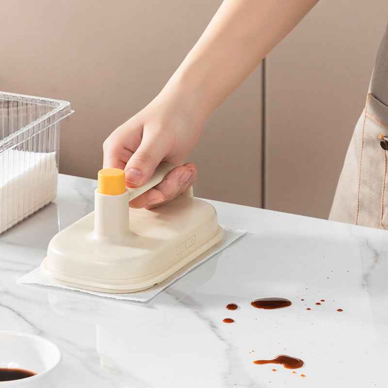 Hand using Petra store Cleaning Magic Brush scrubbing brown stains on white kitchen countertop