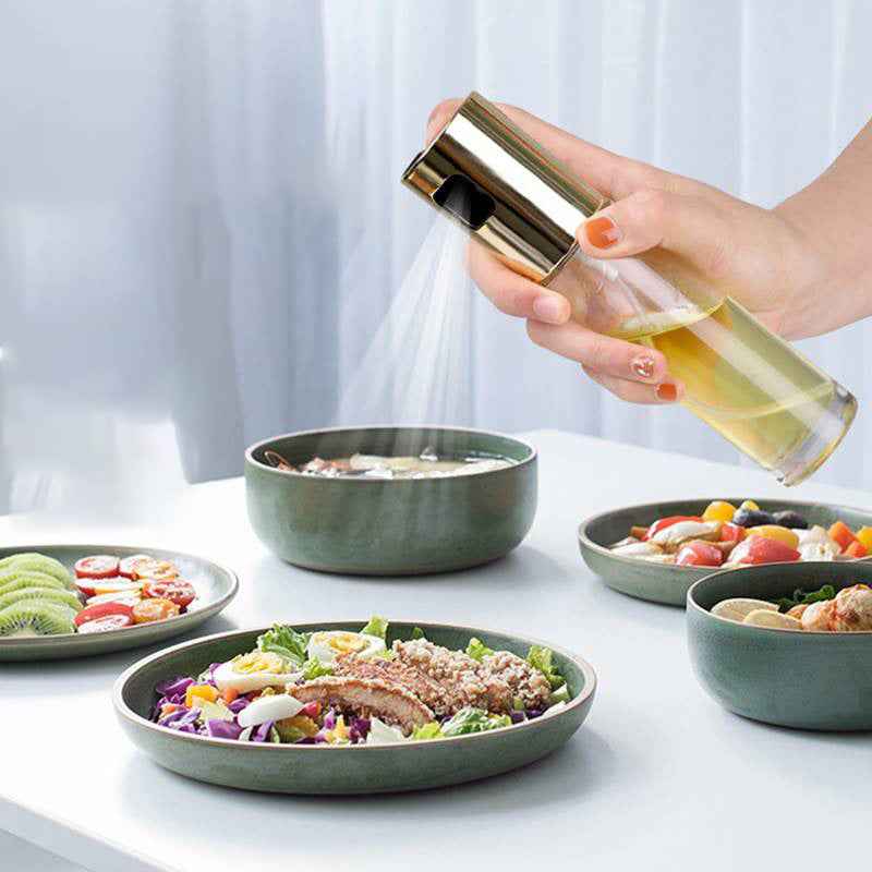 Hand spraying cooking oil from a Petra store Cooking Oil Spray Bottle over a bowl of food in a kitchen setting