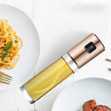 Petra store Cooking Oil Spray Bottle with gold top and clear body next to plates of pasta and meat