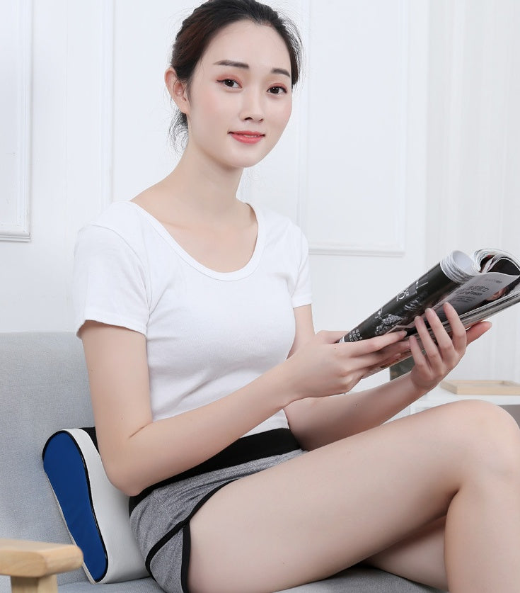 Woman sitting on couch using Petra store massage pillow for back support while reading a magazine