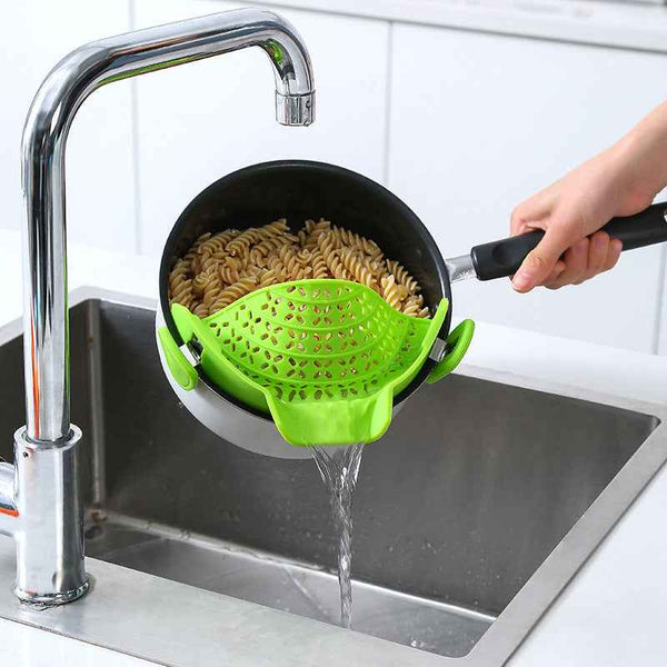 Green Pot Side Drain Stopper attached to black pot draining pasta into stainless steel kitchen sink