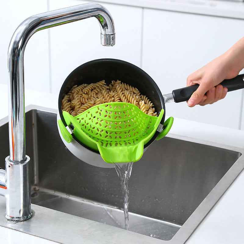 Green Pot Side Drain Stopper attached to black pot draining pasta into stainless steel kitchen sink
